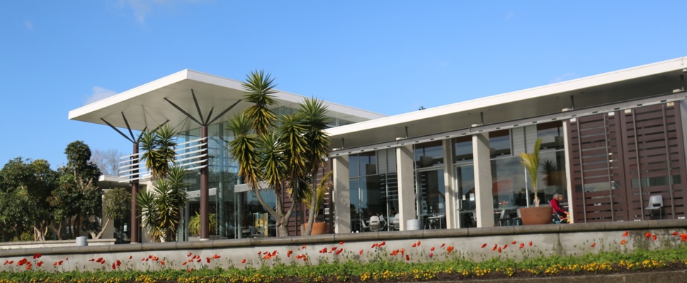 The image shows the visitor centre terrace on a sunny day with chairs and tables under the eaves set up for customers of cafe Miko.  The blooms of red poppies adorn the foreground below the terrace.